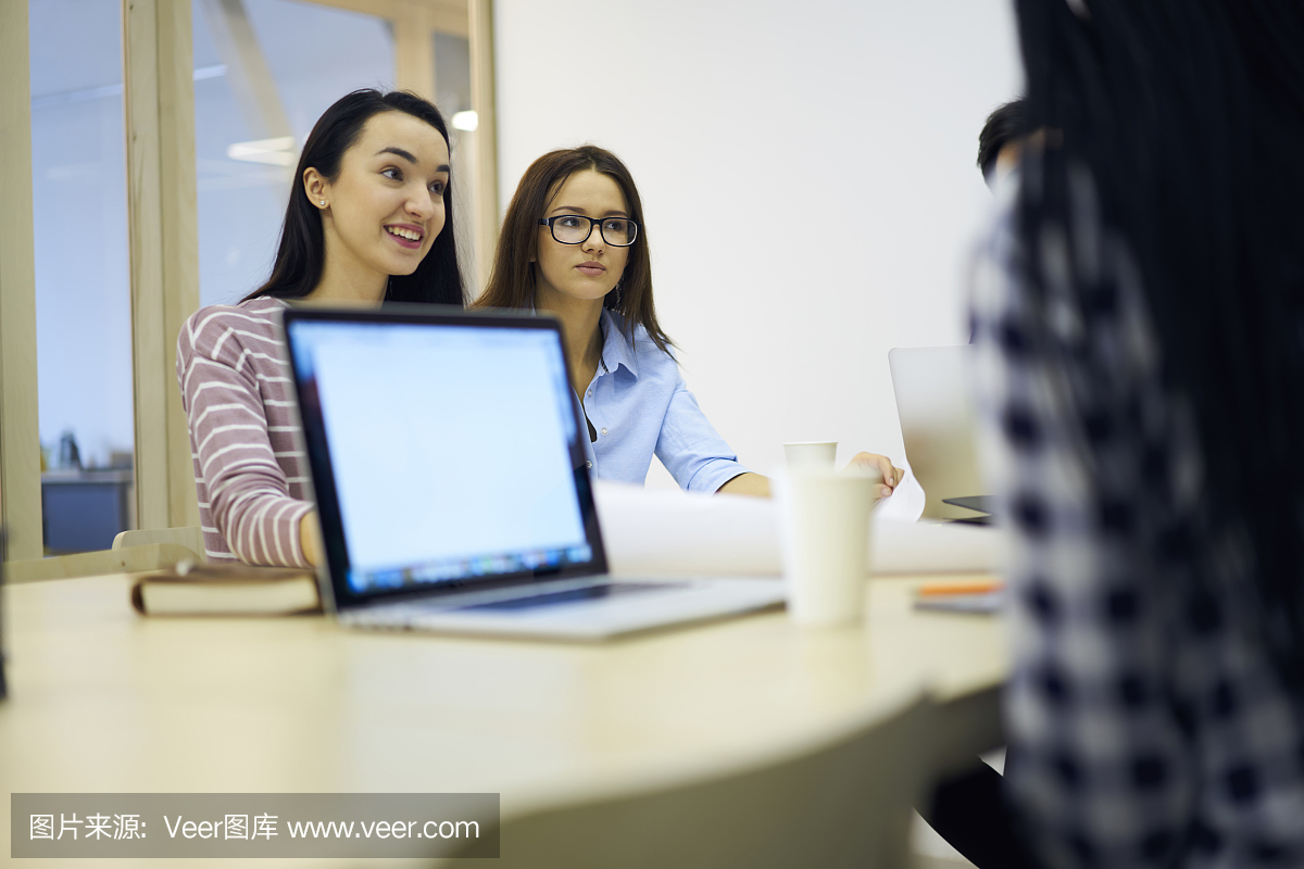 一群才华横溢的学生坐在共同工作的办公室里,在友好的氛围中进行咨询,并通过模拟屏幕连接到无线互联网的笔记本电脑浏览信息